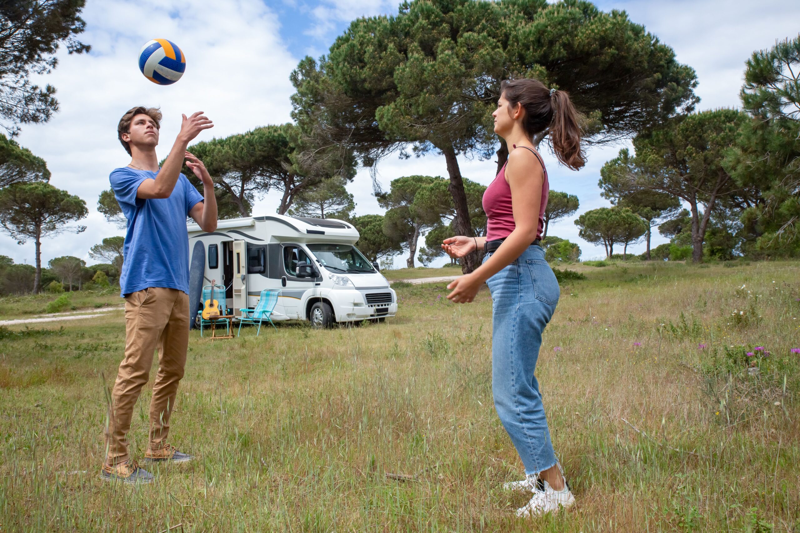 A young couple plays volleyball near their camper van in a scenic outdoor setting in Portugal.